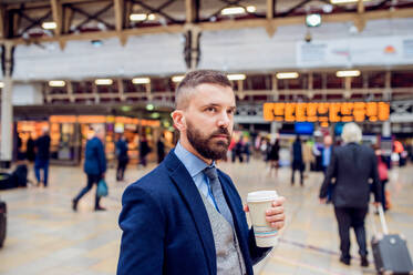 Hipster-Geschäftsmann hält einen Einweg-Kaffeebecher auf dem überfüllten Bahnhof - HPIF35775