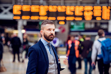 Hipster-Geschäftsmann hält einen Einweg-Kaffeebecher auf dem überfüllten Bahnhof - HPIF35777