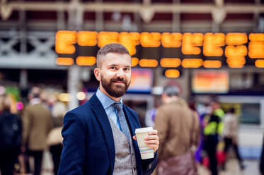 Hipster-Geschäftsmann hält einen Einweg-Kaffeebecher auf dem überfüllten Bahnhof - HPIF35778