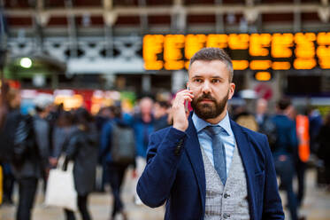 Junger gutaussehender Geschäftsmann mit Smartphone auf dem überfüllten Bahnhof - HPIF35782