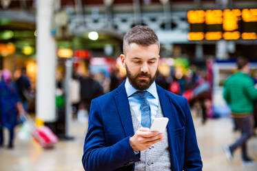 Junger gutaussehender Geschäftsmann mit Smartphone auf dem überfüllten Bahnhof - HPIF35784