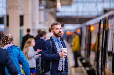 Hipster-Geschäftsmann hält einen Einweg-Kaffeebecher auf dem Bahnsteig - HPIF35787