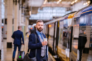 Hipster-Geschäftsmann hält einen Einweg-Kaffeebecher auf dem Bahnsteig - HPIF35788