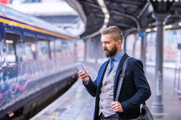 Hipster businessman with smartphone, waiting at the train station platform - HPIF35790