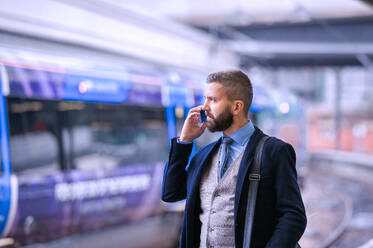 Hipster businessman with smartphone, making a phone call, walking at the train station platform - HPIF35793