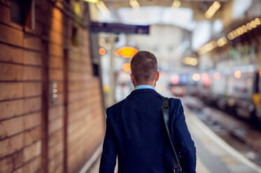 Businessman in suit walking at the train staition platform, back view, rear viewpoint - HPIF35795