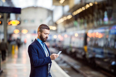 Hipster-Geschäftsmann mit Smartphone, der am Bahnsteig wartet - HPIF35798