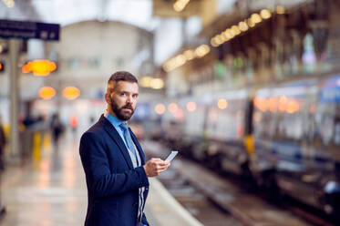 Hipster businessman with smartphone, waiting at the train station platform - HPIF35799