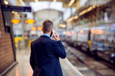 Hipster-Geschäftsmann mit Smartphone, telefonierend, wartend auf dem Bahnsteig, Rückansicht, Rückseite, Blickwinkel - HPIF35800