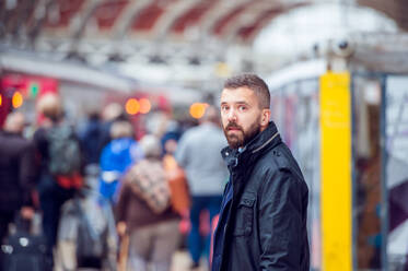 Junger gutaussehender Hipster-Mann in schwarzer Jacke wartet am überfüllten Bahnhof - HPIF35806