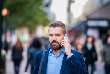 Hipster-Manager, der ein Smartphone in der Hand hält und einen Anruf tätigt, auf einer Straße in London - HPIF35822