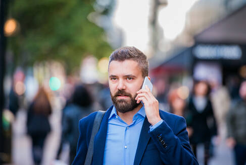 Hipster-Manager, der ein Smartphone in der Hand hält und einen Anruf tätigt, auf einer Straße in London - HPIF35822