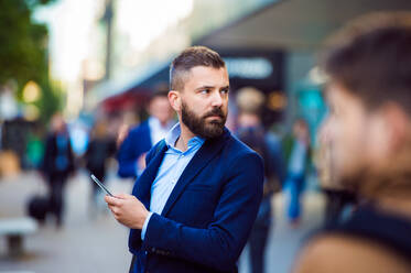 Hipster manager holding a smartphone outside in the crowded street - HPIF35829
