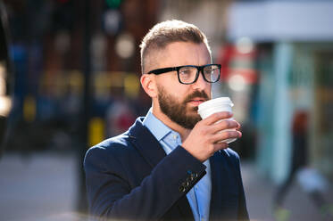 Hipster-Geschäftsmann, der einen Einwegbecher in der Hand hält und Kaffee trinkt, auf der Straße in London, mit schwarzer Brille - HPIF35836