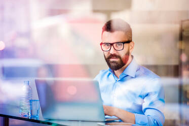 Hipster manager sitting in cafe by the window working on laptop, street reflection - HPIF35850