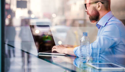 Hipster manager sitting in cafe by the window working on laptop, street reflection - HPIF35853