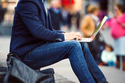 Unbekannter Manager sitzt auf einer Treppe am belebten Piccadilly Circus, London, und arbeitet am Laptop - HPIF35858