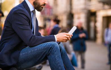 Unbekannter Manager sitzt auf einer Treppe am sonnigen Piccadilly Circus, London, und arbeitet an seinem Smartphone - HPIF35864