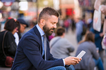 Unbekannter Manager sitzt auf einer Treppe am sonnigen Piccadilly Circus, London, und arbeitet an seinem Smartphone - HPIF35865