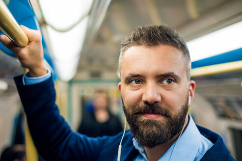Nahaufnahme des Gesichts eines Geschäftsmannes mit Kopfhörern auf dem Weg zur Arbeit, der in einem U-Bahn-Waggon steht und einen Handgriff hält. - HPIF35883