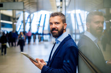 Hipster businessman holding a tablet in his hands, standing on subway station - HPIF35888