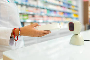 Die Hand einer anonymen Kassiererin, die verschiedene Armbänder trägt, scannt ein Paket mit einem Barcode-Lesegerät in einem Apothekengeschäft - ADSF50370