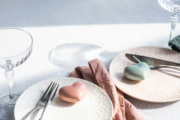 Draufsicht auf einen Keramikteller mit Besteck und Serviette mit herzförmigem Deko-Kristall auf einer Betonfläche am Küchentisch für eine Mahlzeit während der Valentinstagsfeier - ADSF50378