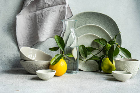 Eine raffinierte Tischdekoration mit feinem Keramikgeschirr, frischen Zitronen und Birnen auf einem strukturierten Leinenhintergrund. - ADSF50381