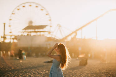 Eine heitere Szene zeigt eine Frau am Santa Monica Pier, mit dem ikonischen Riesenrad im Hintergrund. Der goldene Sonnenuntergang taucht alles in ein warmes Licht. - ADSF50413