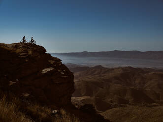 Zwei Mountainbiker mit ihren Fahrrädern auf dem Gipfel einer Klippe mit Blick auf eine weite Landschaft - ADSF50427