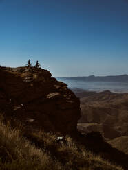 Zwei Mountainbiker mit ihren Fahrrädern auf dem Gipfel einer Klippe mit Blick auf eine weite Landschaft - ADSF50428