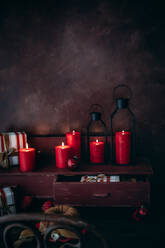 Eine warme, einladende Weihnachtsszene mit leuchtenden roten Kerzen, alten Laternen und rustikalen Holzornamenten vor einem dunklen Hintergrund. - ADSF50442