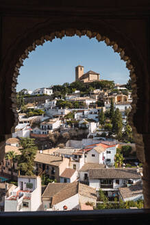 Schöner Blick auf das Stadtbild mit Glockenturm und Wohngebäuden auf einem Hügel gegen den klaren Himmel, gesehen durch das Bogenfenster des Generalife-Palastes in Granada, Spanien - ADSF50448