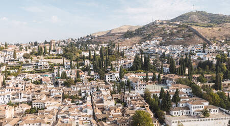 Schöner Blick auf das Stadtbild mit Wohngebäuden und Bäumen auf einem Hügel gegen den bewölkten blauen Himmel in Granada, Spanien - ADSF50450