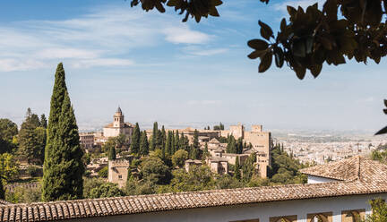 Schöner Blick auf den historischen Alhambra-Palast, umgeben von üppigen grünen Bäumen und blauem Himmel an einem bewölkten Tag in Andalusien, Granada, Spanien - ADSF50452