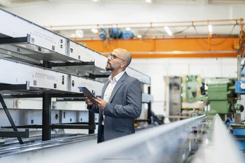 Businessman examining machinery and holding tablet PC in factory - DIGF21018