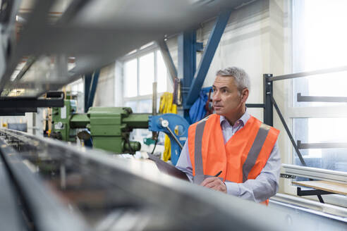 Engineer examining machine and preparing checklist in factory - DIGF21020