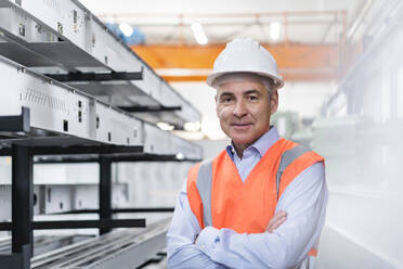 Smiling engineer standing with arms crossed near machinery in factory - DIGF21032