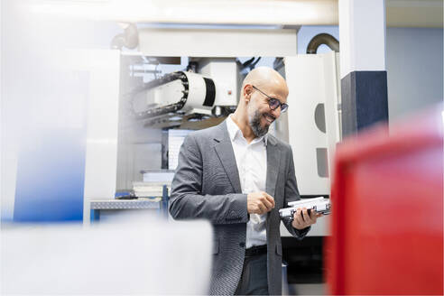 Smiling businessman examining machine part in factory - DIGF21033