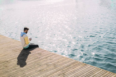 Man sitting and using smart phone on pier near sea - EGHF00816