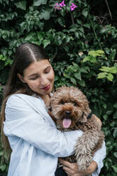 Smiling young woman with poodle dog in front of plants - GDBF00117