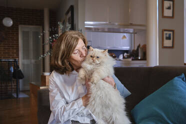 Woman embracing Persian cat and sitting on sofa at home - MMPF01089