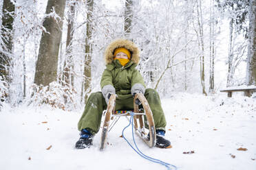 Boy sitting on sled at winter forest - NJAF00710