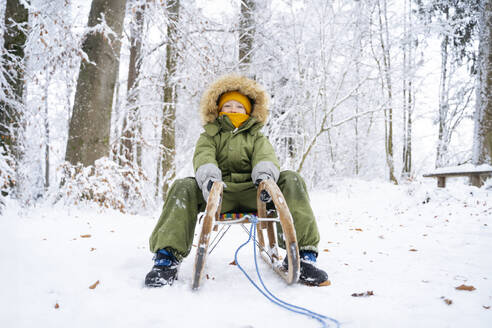 Boy sitting on sled at winter forest - NJAF00710