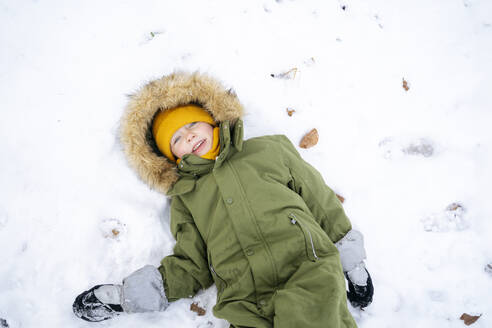 Happy boy lying on snow in winter - NJAF00711