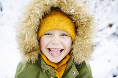 Playful boy wearing parka coat and sticking out tongue - NJAF00713