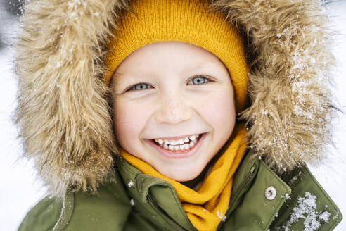 Happy boy wearing parka coat in snow - NJAF00717