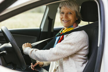 Lächelnde reife Frau, die den Sicherheitsgurt im Auto anlegt - EBSF04285