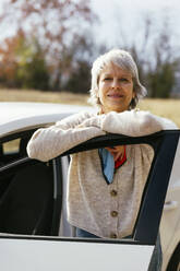 Smiling woman leaning on car door - EBSF04296