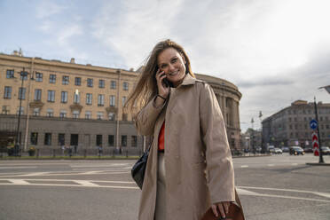 Lächelnde Frau, die vor einem Gebäude mit ihrem Handy telefoniert - VPIF09034